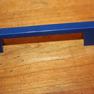 May include: A blue plastic drawer pull with a rectangular shape and rounded edges.