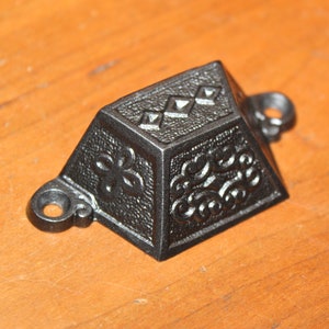 May include: Black metal decorative hardware with intricate floral and geometric designs. The hardware has two holes for mounting.