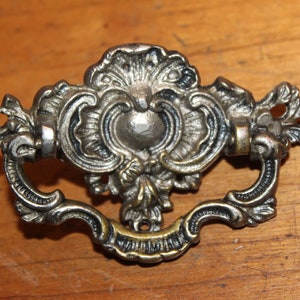 May include: Ornate silver-toned metal drawer pull with a decorative floral design.