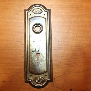 May include: A vintage brass door plate with a keyhole and a decorative floral design.