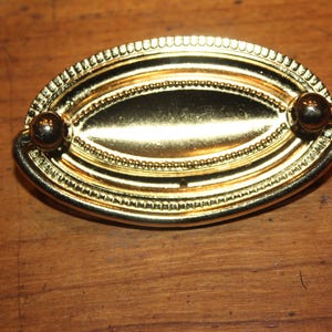 May include: A gold oval-shaped cabinet pull with a beaded border and two round knobs.