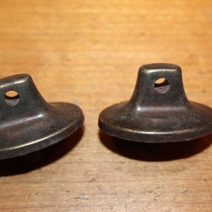 May include: Two antique brass-colored metal furniture feet with a round base and a square top with a hole in the center.
