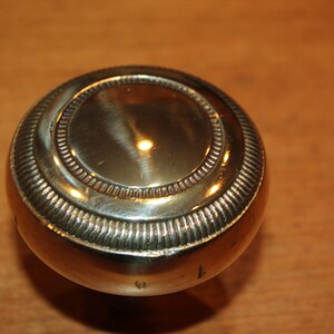 May include: A round, polished brass door knob with a decorative, raised rim.