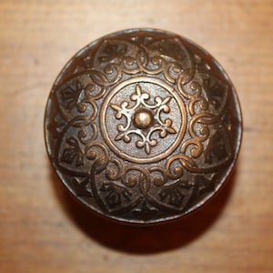 May include: A round, ornate, brass door knob with a detailed floral design.