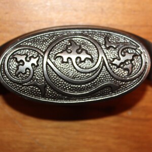 May include: A silver-toned metal cabinet pull with an oval shape and a decorative design of swirling leaves and vines.