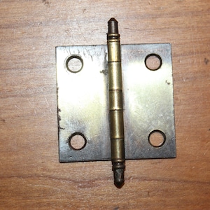 May include: A brass hinge with two holes on each side and a decorative pin in the center.