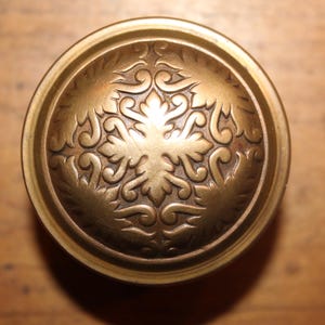 May include: A round, brass door knob with an intricate, floral design.