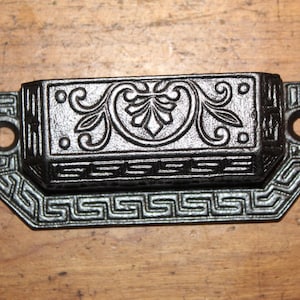 May include: Black cast iron drawer pull with a decorative floral design and a geometric border.