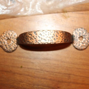 May include: A hammered copper cabinet pull with a decorative, pointed design on each end.