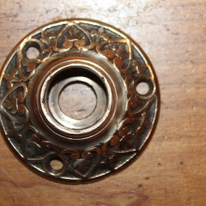 May include: A brass door knob rosette with an intricate floral design. The rosette has three holes for mounting.
