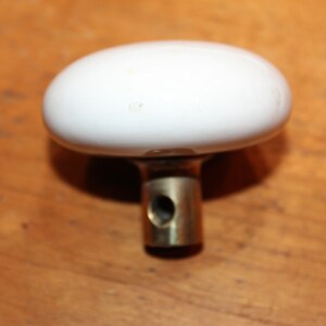 May include: White ceramic door knob with a brass base. The knob is oval shaped and has a smooth finish.