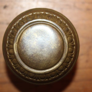 May include: A brass door knob with a decorative, ornate design. The knob has a circular shape with a raised, textured rim.
