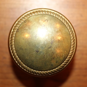 May include: A round, gold-colored door knob with a rope-like design around the edge.