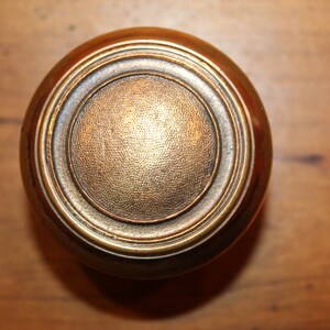 May include: A round, brass door knob with a concentric circle design.
