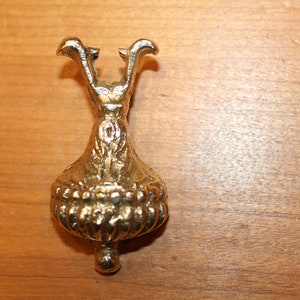 May include: A gold metal furniture leg with an ornate design. The leg has a round base and a pointed top.