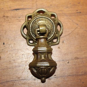 May include: A brass cabinet pull with a decorative, ornate design. The pull has a round, openwork base and a bulbous, fluted handle.