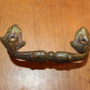 May include: A vintage brass drawer pull with a decorative floral design. The pull has a curved shape and a smooth finish.