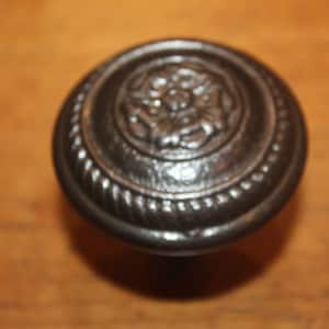 May include: A black metal door knob with a decorative design. The knob has a rope-like border and a floral design in the center.