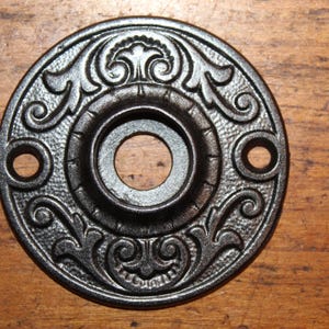 May include: A black cast iron door knob rosette with an ornate floral design.