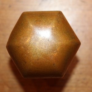 May include: A hexagonal brass knob with a smooth, slightly textured surface. The knob is a warm, golden color.