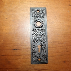 May include: A vintage, ornate, silver-colored door plate with a keyhole and intricate floral designs.