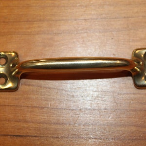 May include: A brass door pull with a rounded handle and square ends. The pull has two holes on each end.