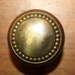 May include: A round, brass door knob with a beaded edge.
