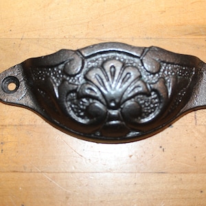 May include: Black cast iron drawer pull with a decorative floral design. The pull has two holes for mounting.