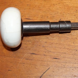 May include: A white ceramic door knob with a black metal rod. The knob has a textured surface.