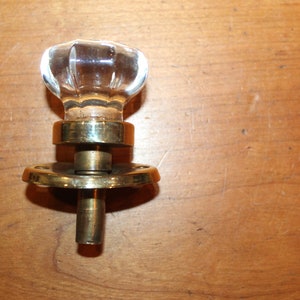 May include: A clear glass door knob with a brass base and a round plate. The knob has a faceted design.