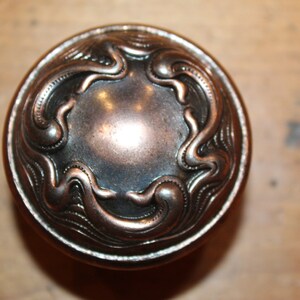 May include: A round, antique-style door knob with a decorative, swirling design. The knob is made of metal and has a dark, aged finish.