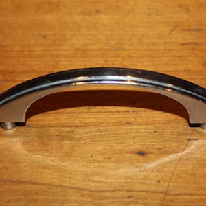 May include: A silver-toned, arched cabinet pull with rounded edges and a smooth finish.