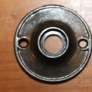 May include: A round, black metal door knob escutcheon with two small holes on the side.