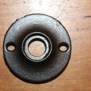 May include: Black metal door knob rosette with two holes for screws. The rosette has a smooth, slightly textured surface.
