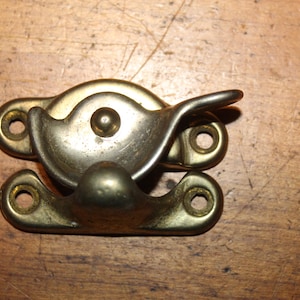 May include: A vintage brass window sash lock with a curved handle and two mounting plates. The lock is made of brass and has a tarnished finish. The lock is designed to secure a window sash.
