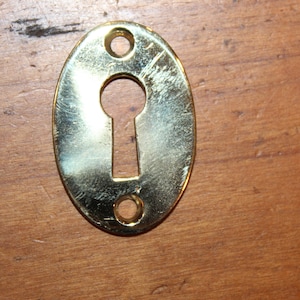 May include: A gold oval-shaped keyhole cover with two small holes on the sides.