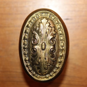May include: A gold oval-shaped door knob with an ornate floral design.