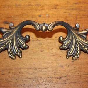 May include: A decorative brass drawer pull with a leaf design. The pull is ornate and has a vintage style.