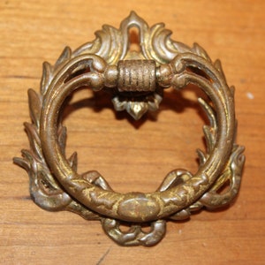 May include: A vintage ornate brass drawer pull with a ring handle and intricate floral designs.