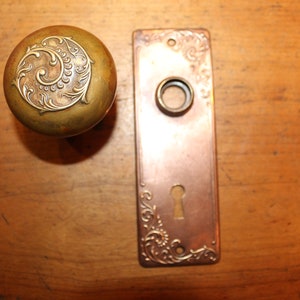 May include: A vintage brass door knob with a decorative floral design and a matching brass door plate with a keyhole.