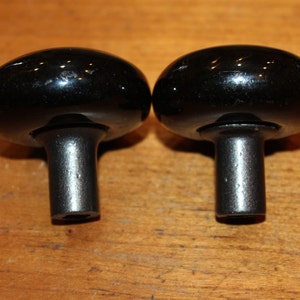 May include: Two black ceramic door knobs with a shiny finish. The knobs are round with a short, cylindrical stem.