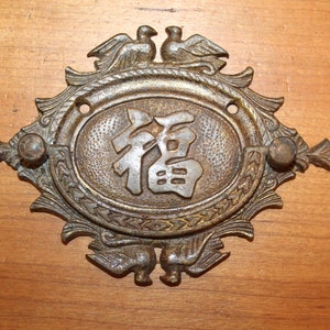 May include: A brass plaque with a decorative design featuring two birds and a Chinese character for "fortune" in the center.