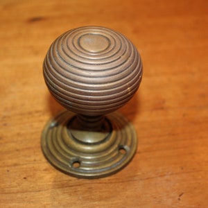 May include: A brass door knob with a round, ribbed design. The knob is attached to a round base with a decorative ring.