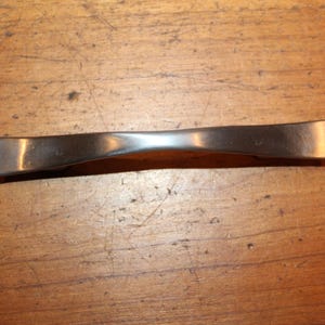 May include: A silver-toned cabinet pull with a curved design.