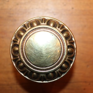 May include: A round, brass door knob with a decorative, ornate design. The knob has a smooth, polished surface.