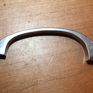May include: A silver metal cabinet pull with a curved shape.