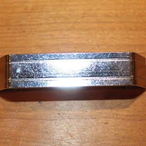 May include: A silver metal drawer pull with a rectangular shape and a slightly curved top. The pull has a smooth, polished finish and a subtle, raised design.