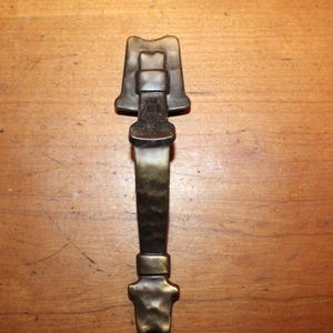 May include: A hammered brass door handle with a decorative top in the shape of a house.