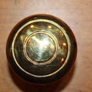 May include: A shiny gold door knob with a circular design.