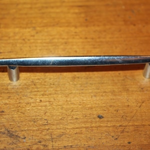May include: A silver cabinet pull with a straight, flat design and rounded ends.